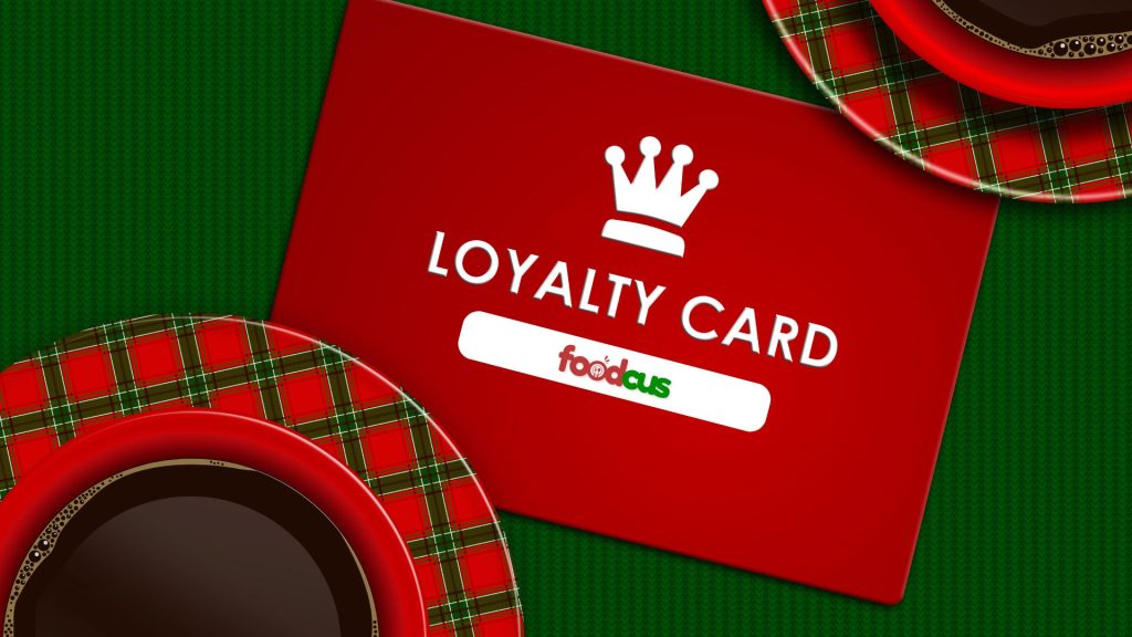 Red loyalty card with a crown icon and Foodcus logo placed beside festive coffee cups and saucers, symbolizing customer rewards and retention.