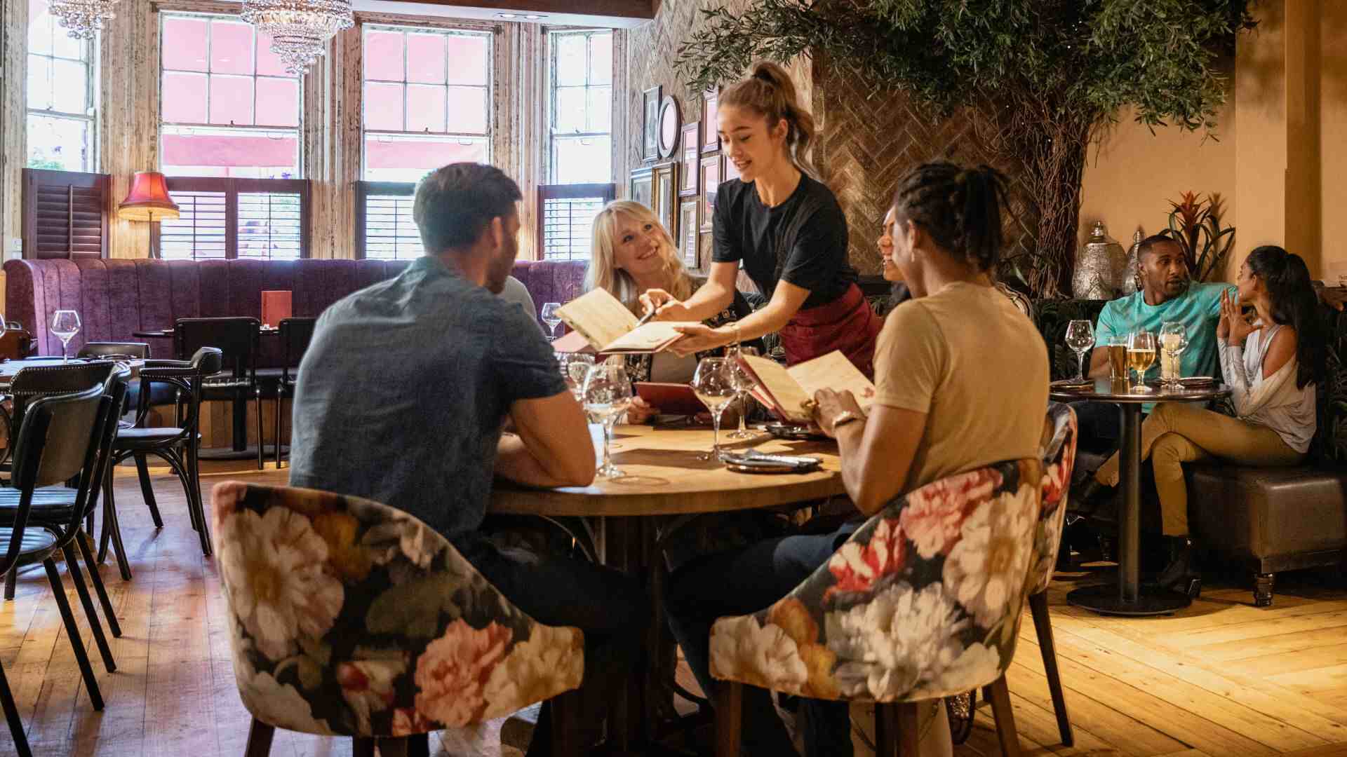 Server assisting a group of guests at a cozy restaurant, showcasing personalized dining service and menu recommendations
